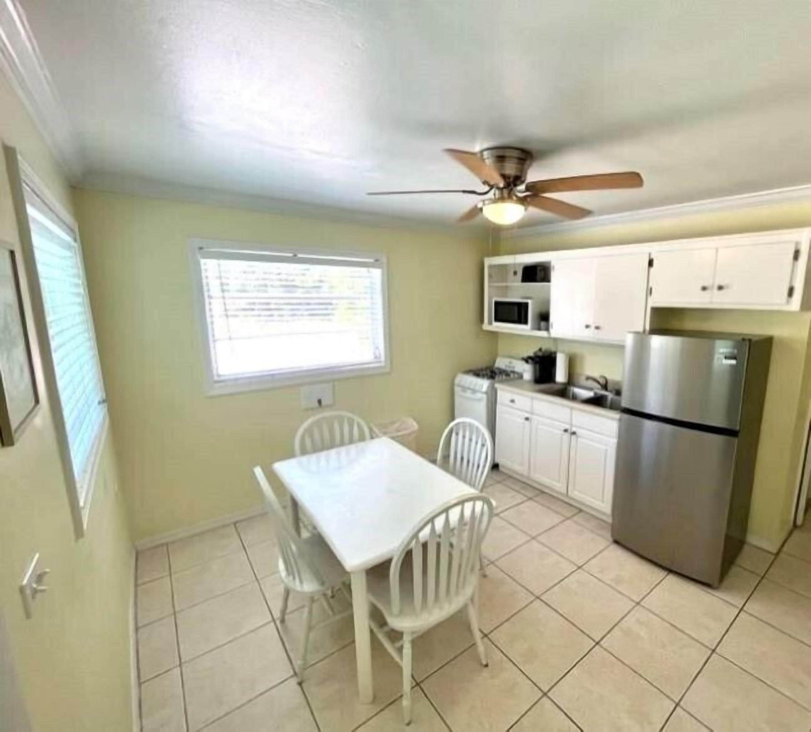 A compact kitchen with white cabinets, a stainless steel refrigerator, a microwave, and a ceiling fan.
