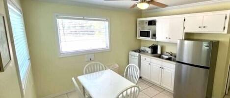 A compact kitchen with white cabinets, a stainless steel refrigerator, a microwave, and a ceiling fan.