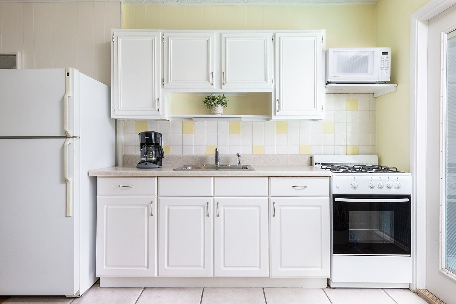 A kitchen with white cabinets, a microwave, a coffee maker, and a stove.