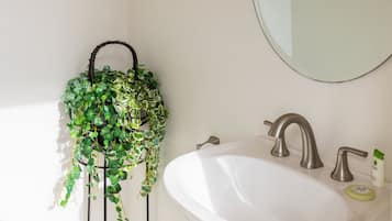 A bathroom with a white sink, a round mirror, and a plant on a stand.