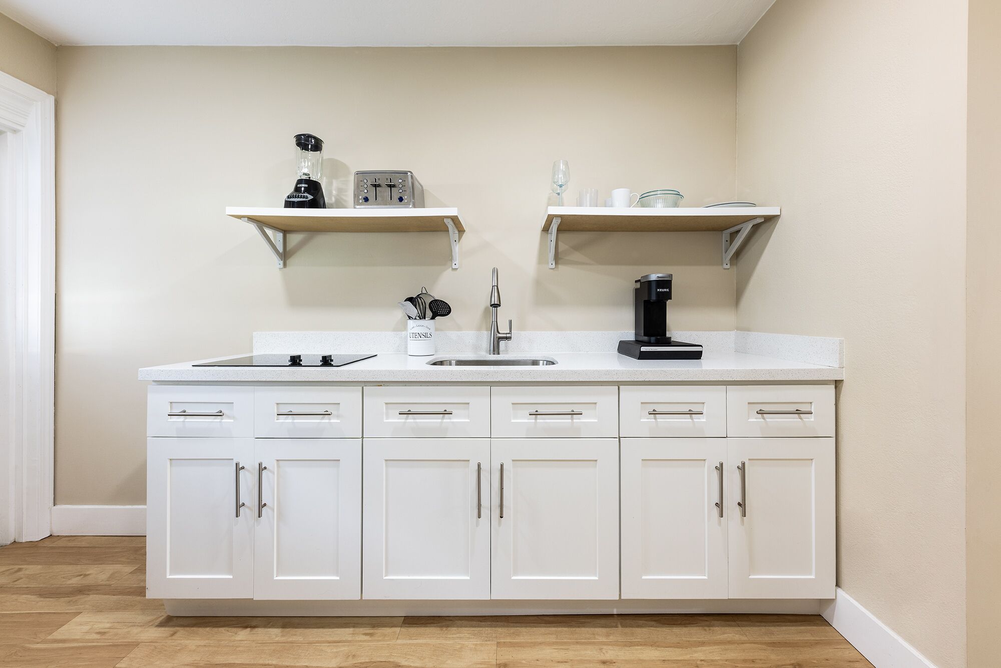 A kitchen with white cabinets, a countertop, a sink, and two wall-mounted shelves with kitchen items.