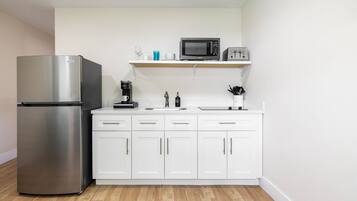 Una cocina compacta con refrigerador de acero inoxidable, microondas, cafetera y armarios blancos.