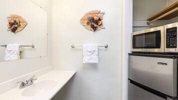 Un baño con lavabo, espejo, toallero y un microondas sobre el lavabo.