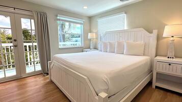 A bedroom with a large bed, two bedside tables with lamps, a sliding glass door, and a view of the outdoors.