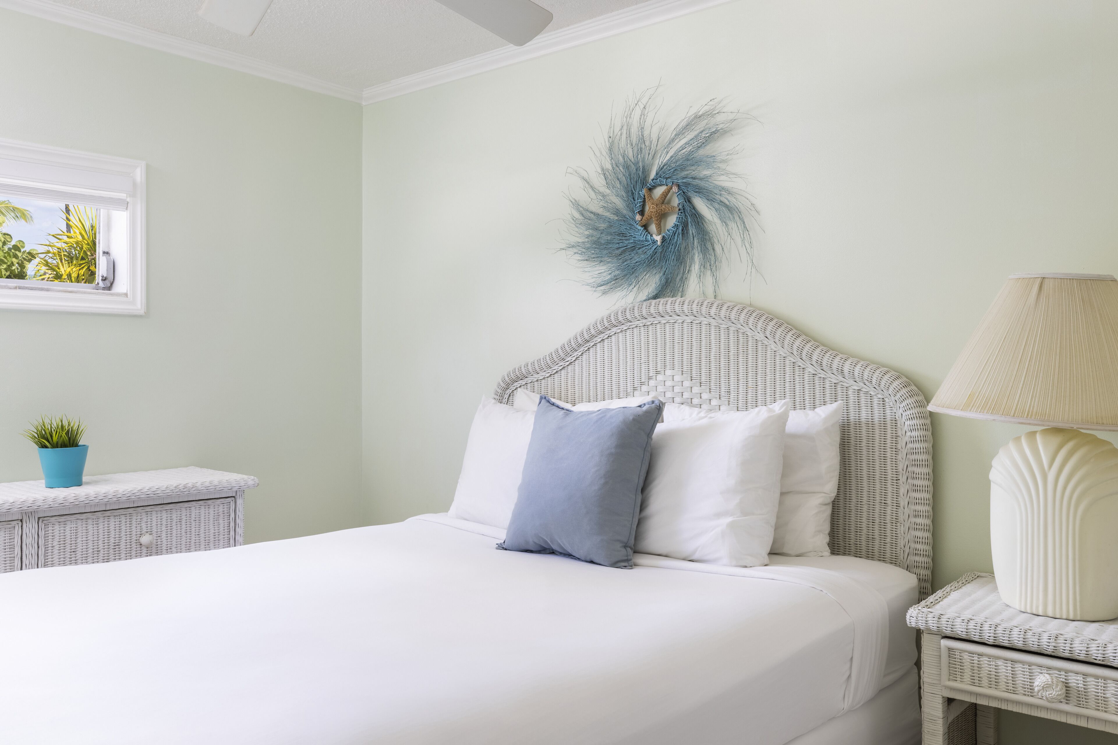 A neatly made bed with white bedding, a wicker headboard, and a decorative feather accent.