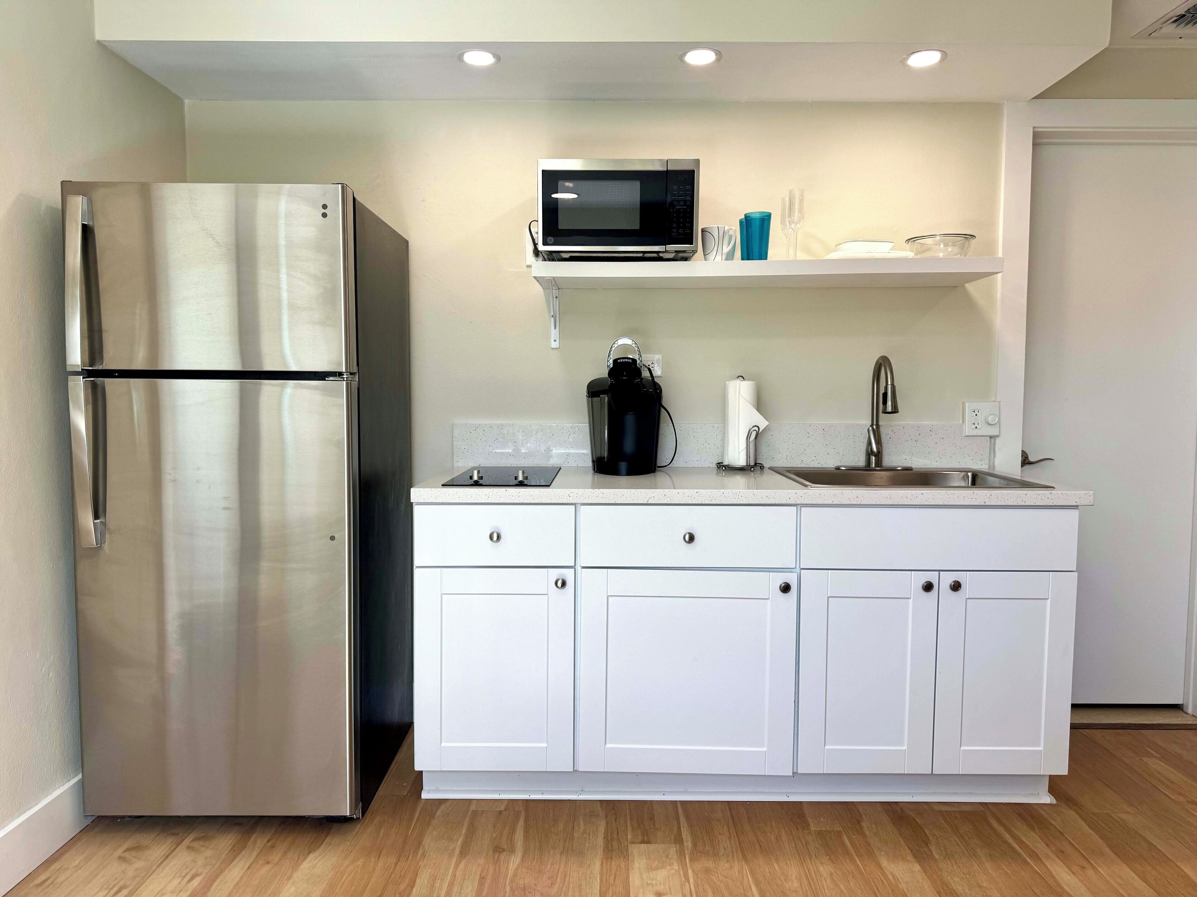 Una cocina moderna con armarios blancos, un refrigerador de acero inoxidable, un microondas, una cafetera y un fregadero.