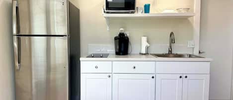 Una cocina moderna con armarios blancos, un refrigerador de acero inoxidable, un microondas, una cafetera y un fregadero.