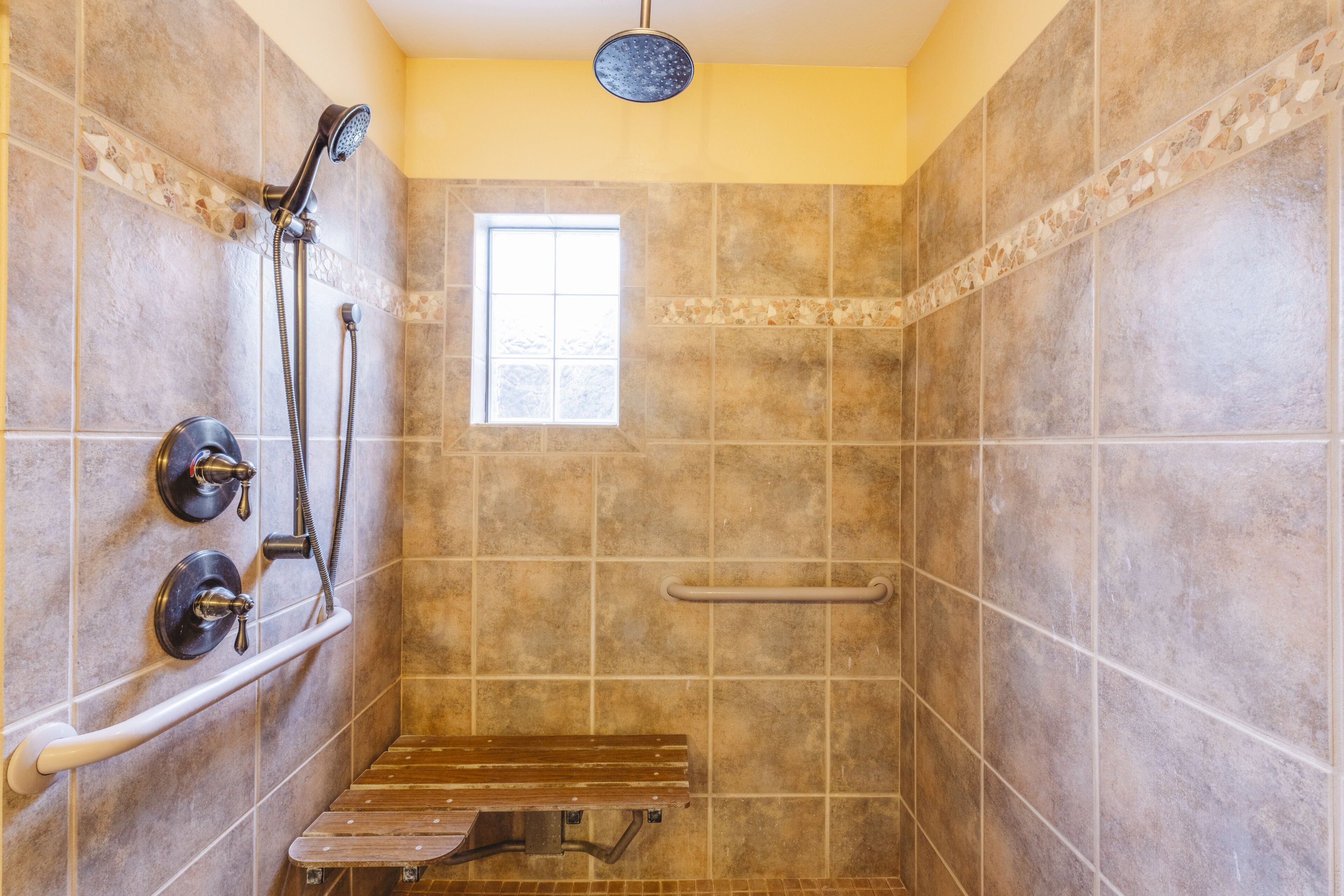 A shower with a bench, grab bars, and a window.