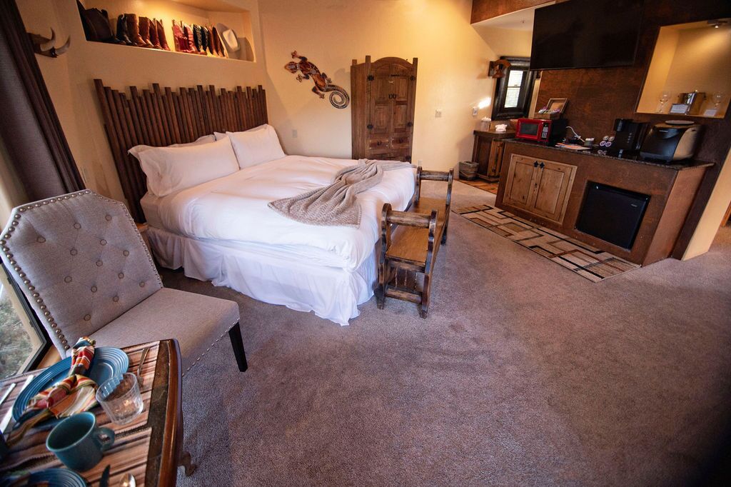 A cozy room with a large bed, a wooden chair, a small table with dishes, and a kitchenette area.