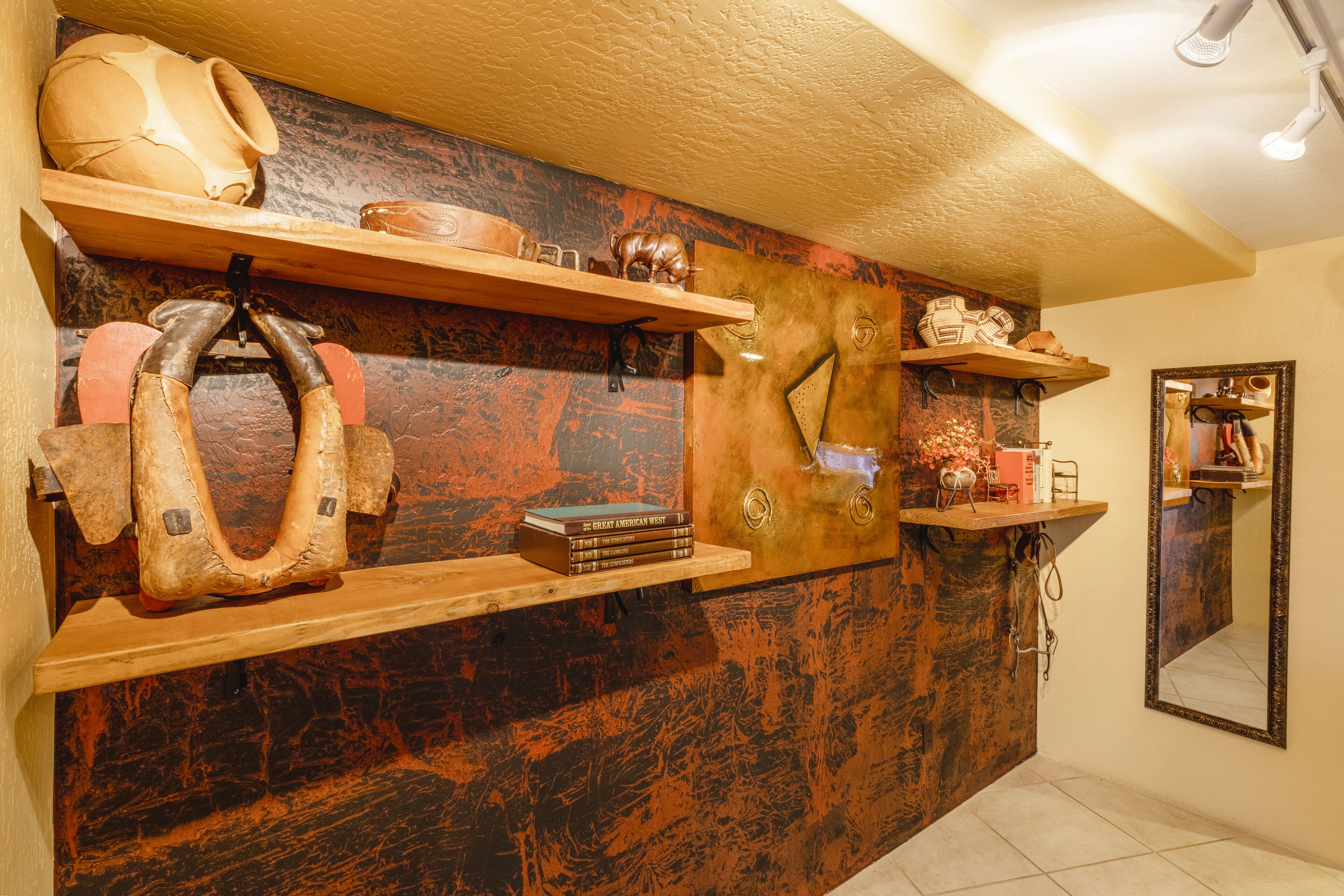 A room with a rustic wall design, wooden shelves with various items, and a mirror.