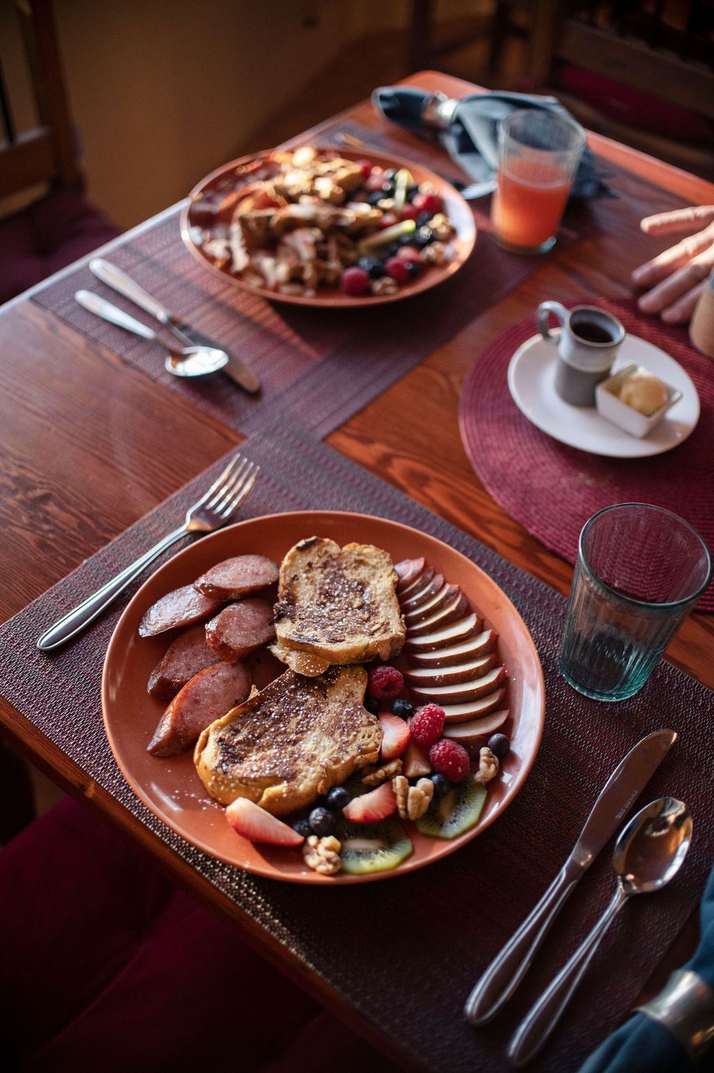 Disposição de café da manhã com torradas, linguiça e frutas vermelhas, um copo de suco e uma xícara de café sobre uma mesa de madeira.