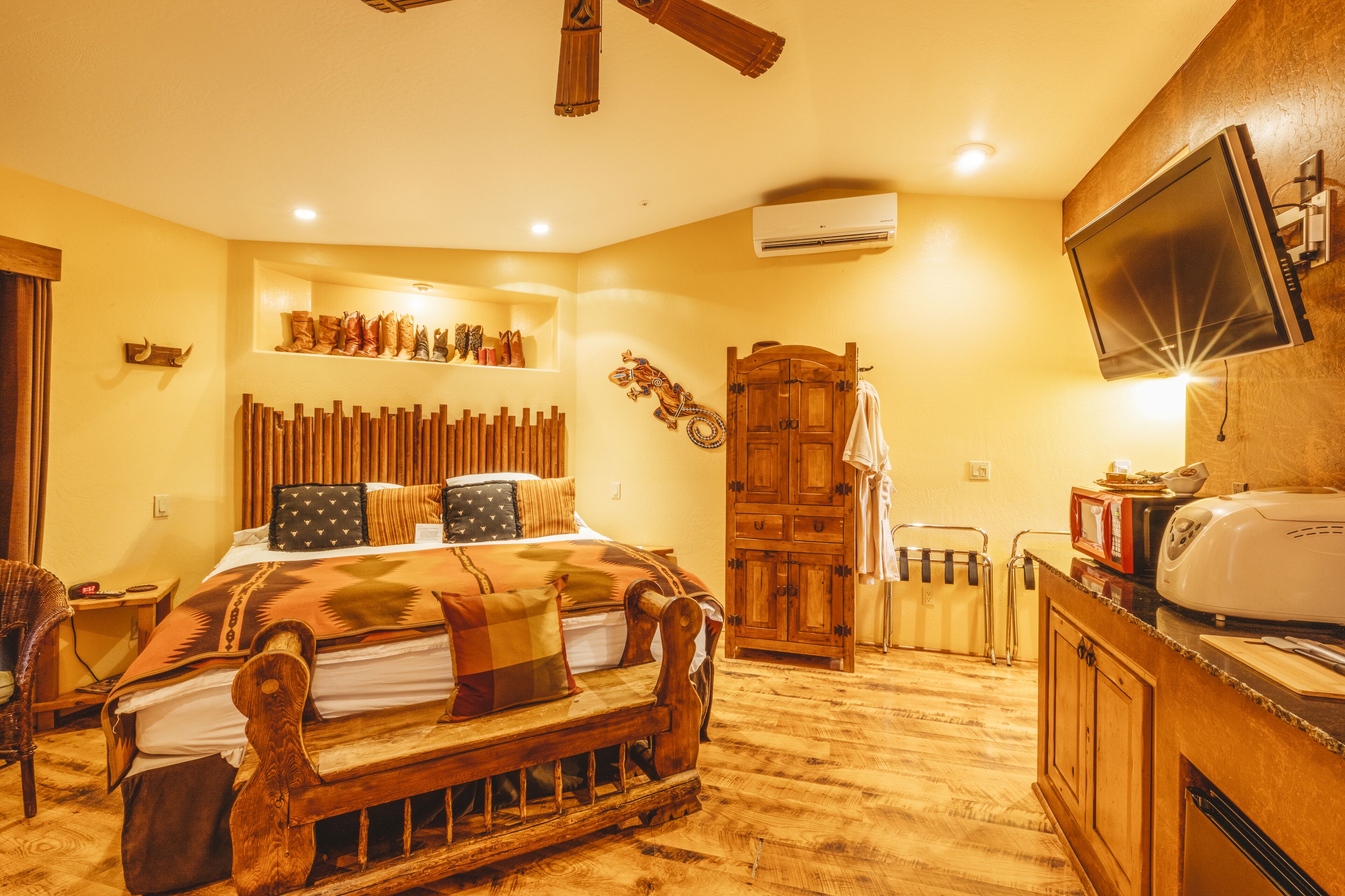 A bedroom with a wooden bed, a wooden wardrobe, a television mounted on the wall, and a shelf with boots.
