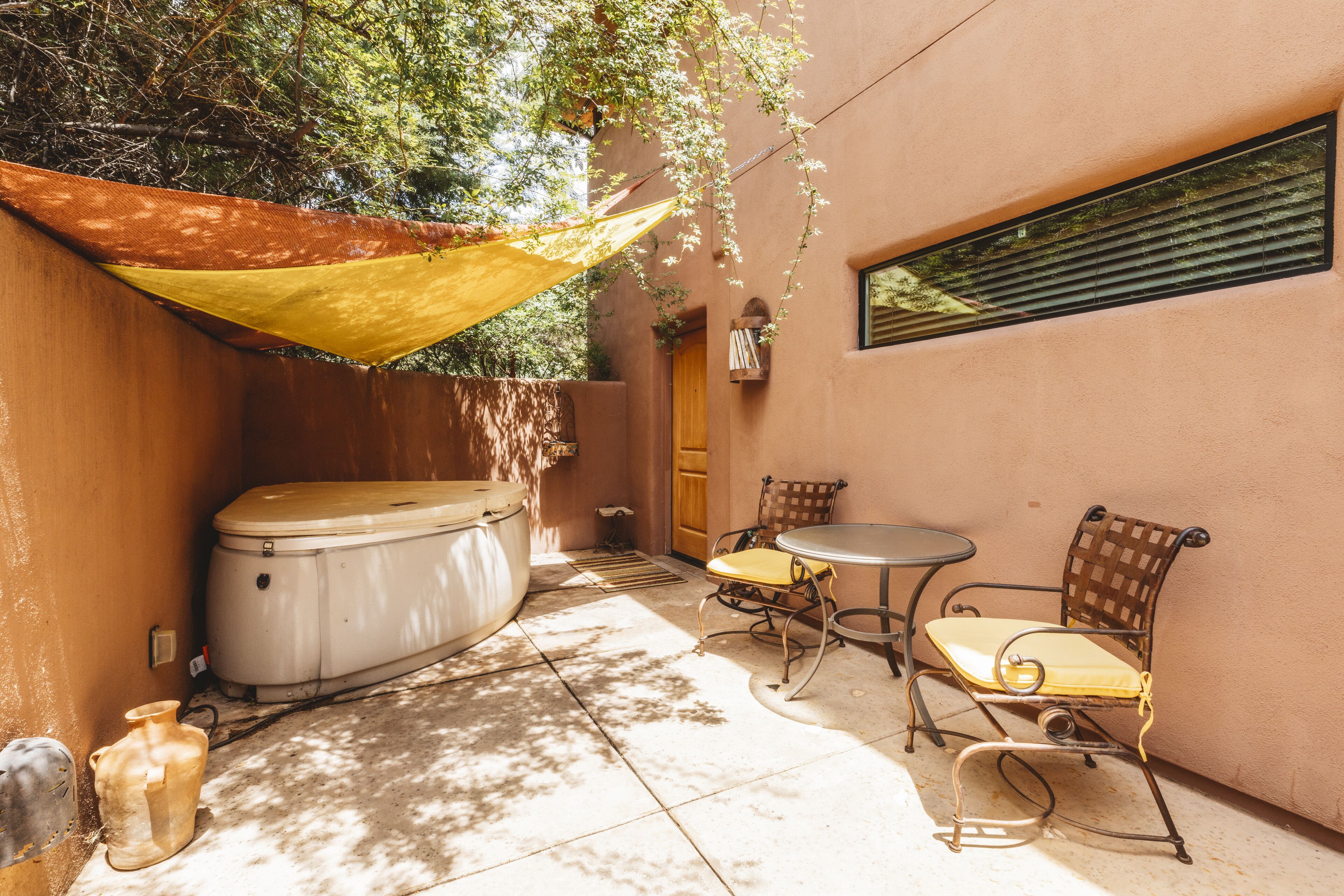 A patio area with a hot tub, two chairs, a table, and a hanging plant.