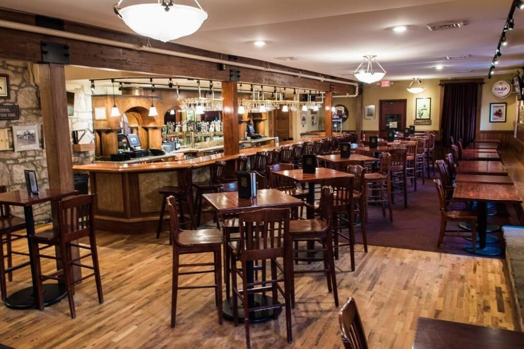 A restaurant with wooden tables and chairs, a bar area with a counter and bar stools, and a stone wall.