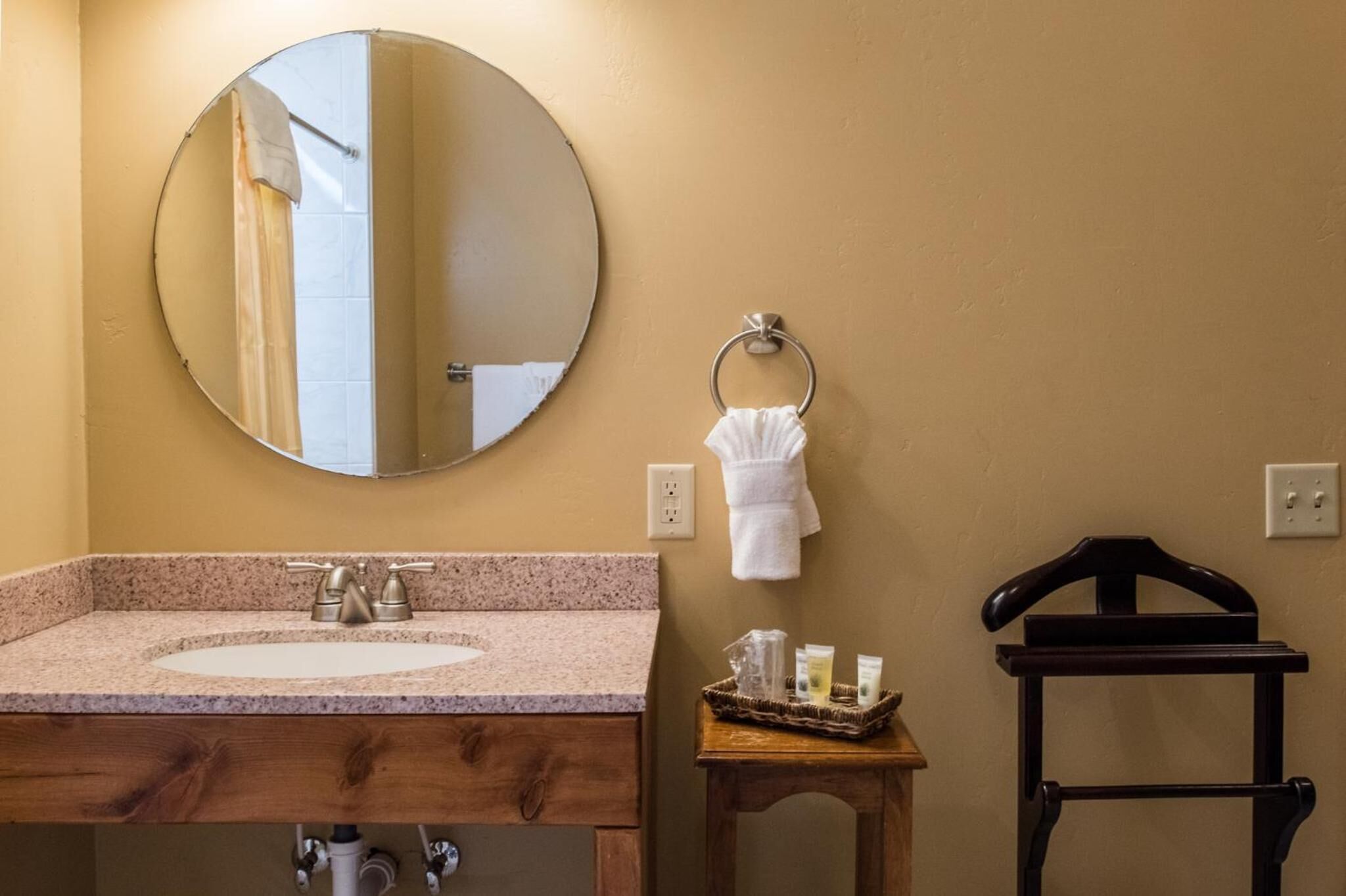 A bathroom with a round mirror, a sink, a towel rack, and a small wooden stool.