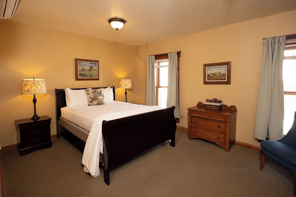A bedroom with a large bed, two bedside tables with lamps, a dresser, and a chair.