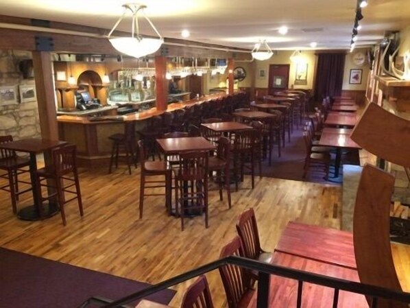 Un restaurante con piso de madera, varias mesas y sillas, una zona de bar y lámparas colgantes.