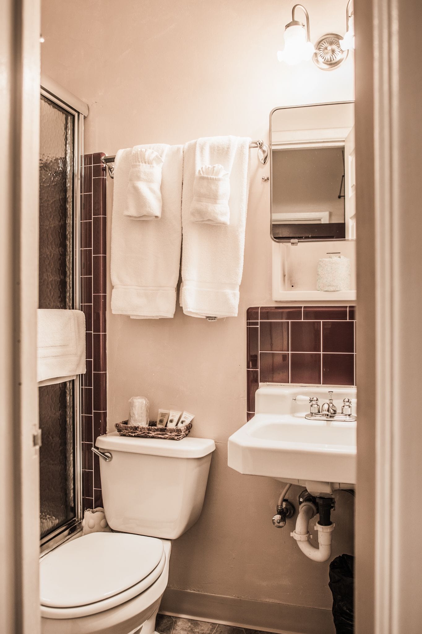 A bathroom with a toilet, sink, and a mirror above the sink. There are towels hanging on a rack.