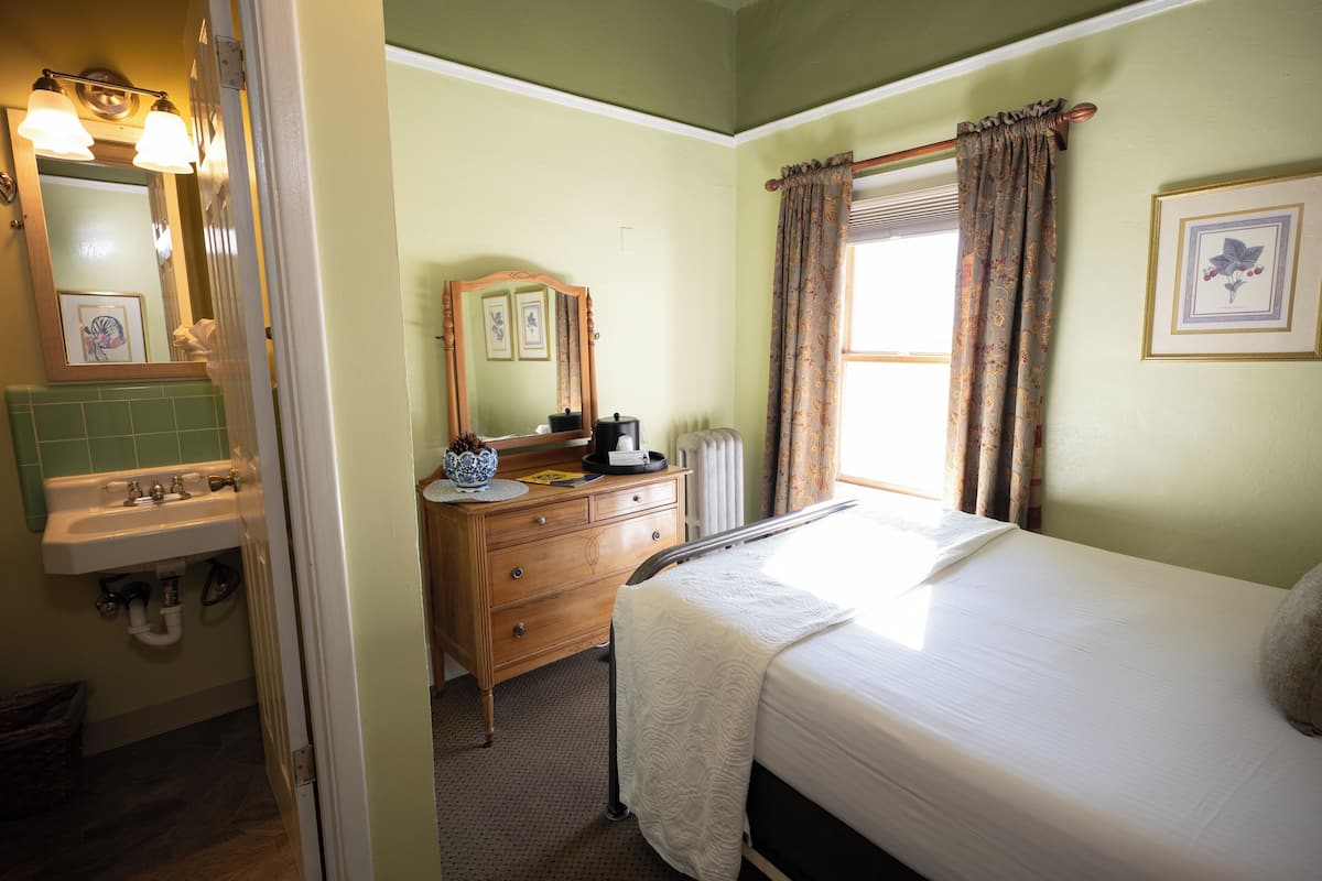 A bedroom with a bed, a dresser, a mirror, and a window with curtains.