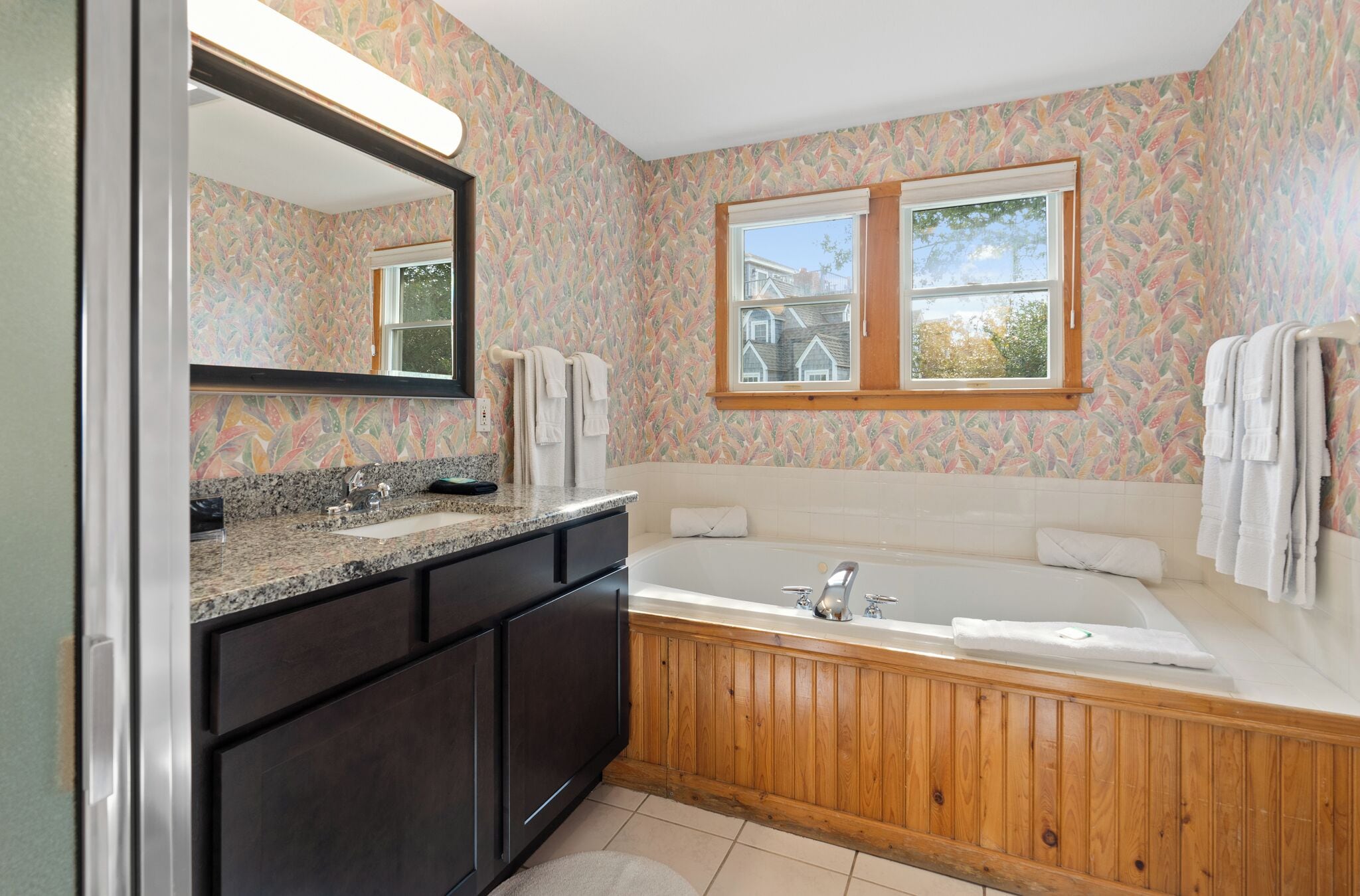 A bathroom with a wooden bathtub, a large mirror, and a window.