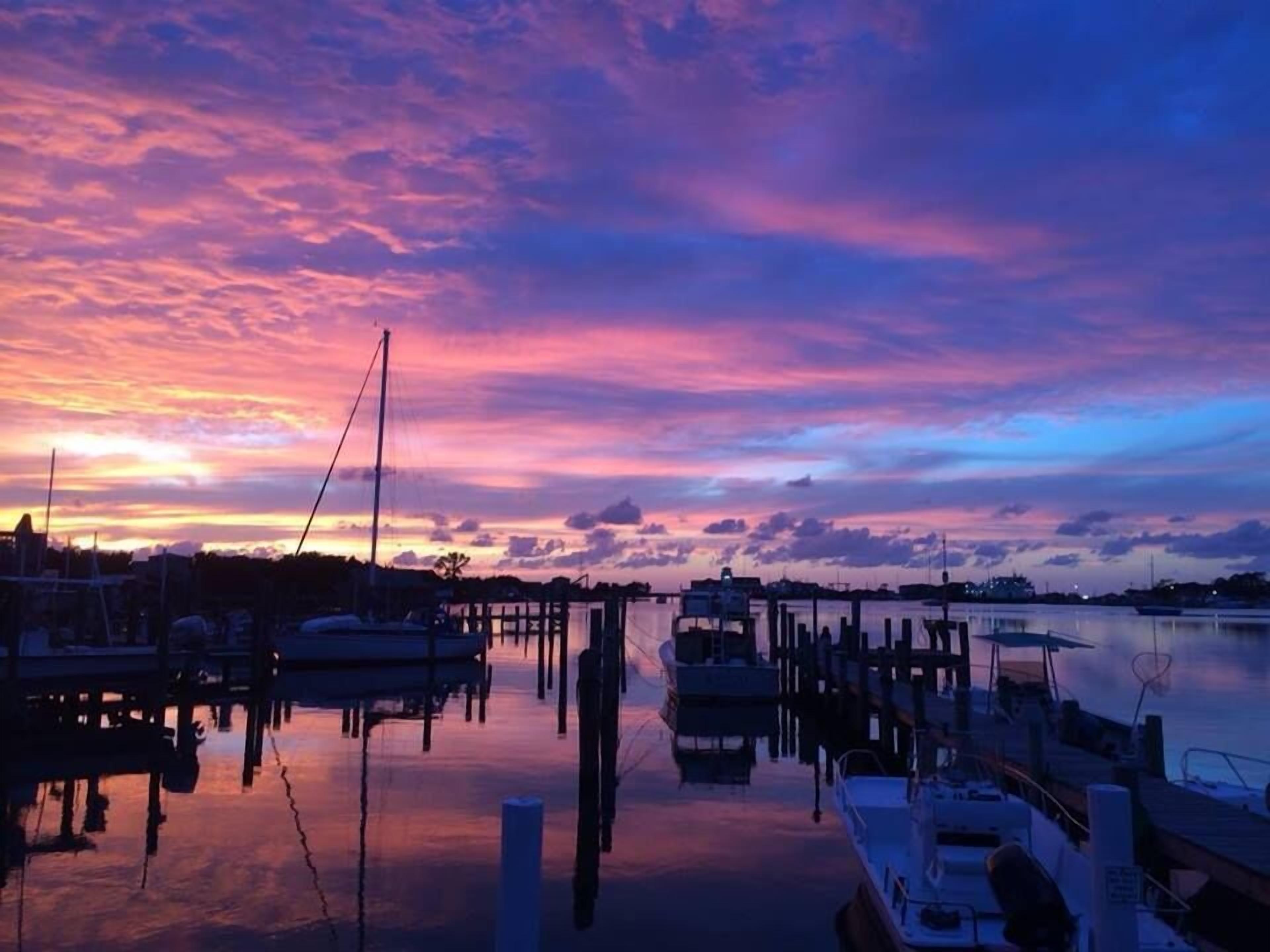 Ein Yachthafen mit Booten, die an hölzernen Stegen vor Anker liegen, wobei der Himmel in Abendrot spiegelt.