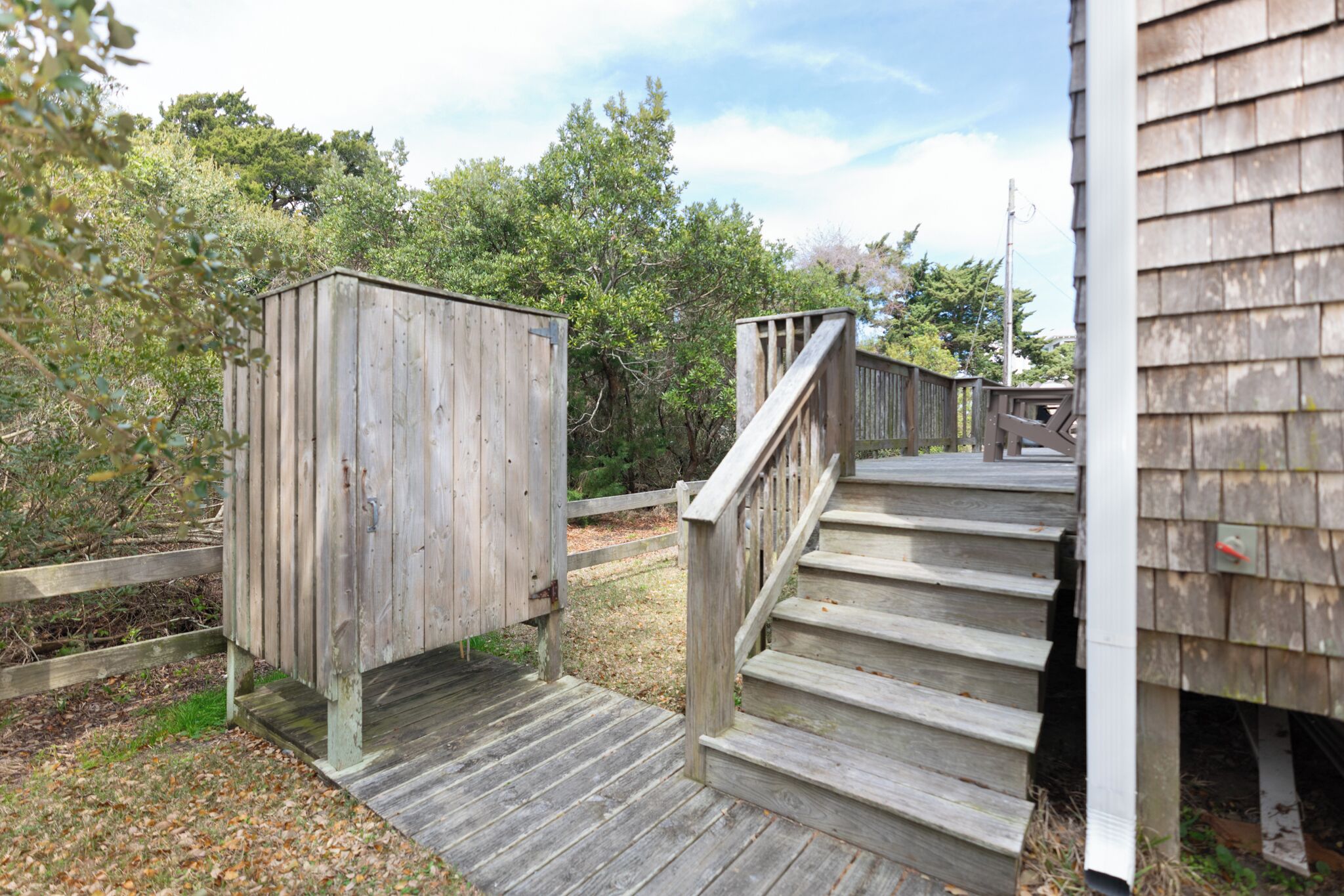 A wooden outdoor staircase leading to a wooden structure, surrounded by trees and a wooden fence.