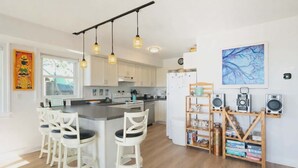 A modern kitchen with a central island, white cabinetry, pendant lighting, and a bookshelf with audio equipment. - Ocracoke Harbor Inn (Ocracoke)