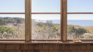 A window with a view of a coastal landscape, wooden window frame, and a small dish on the sill. - Ocracoke Harbor Inn (Ocracoke)