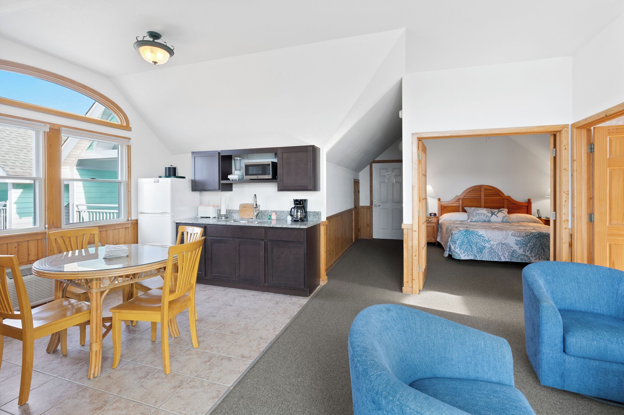 Una habitación compacta con una mesa de comedor, sillas, kitchenette, cama y un ventanal grande.