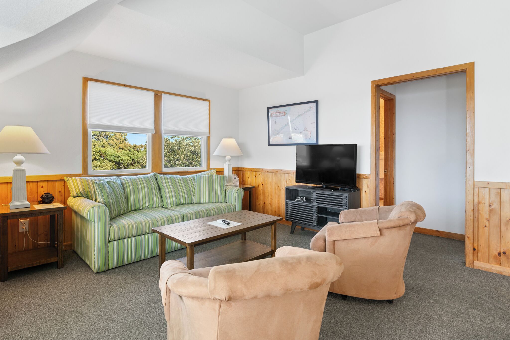 A room with a green-striped sofa, a beige armchair, a wooden coffee table, a TV, and a framed map on the wall.