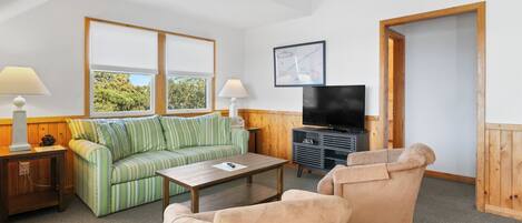 A room with a green-striped sofa, a beige armchair, a wooden coffee table, a TV, and a framed map on the wall.