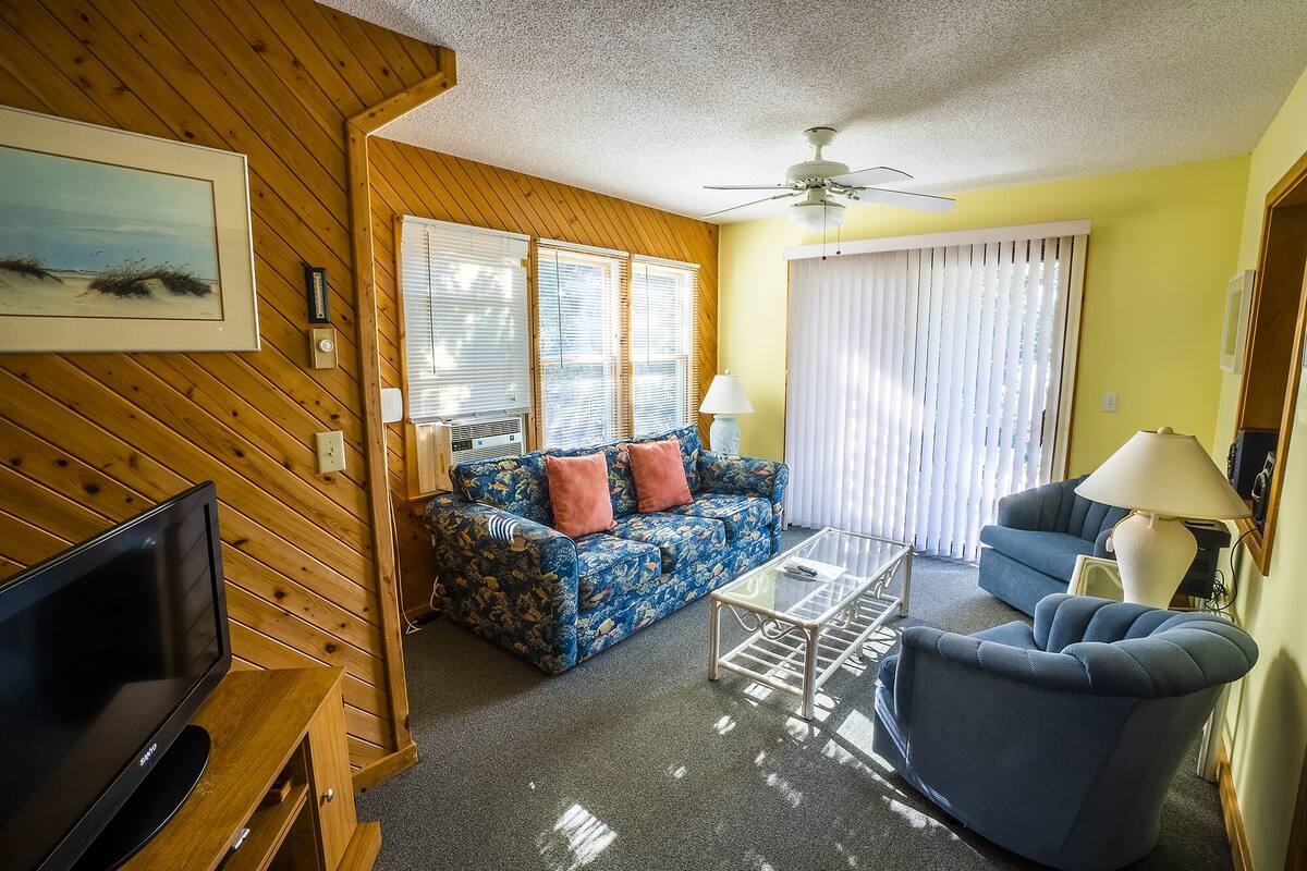 Ein Wohnzimmer mit Fernseher, Sofa und Sessel, Holzwänden und Deckenventilator.
