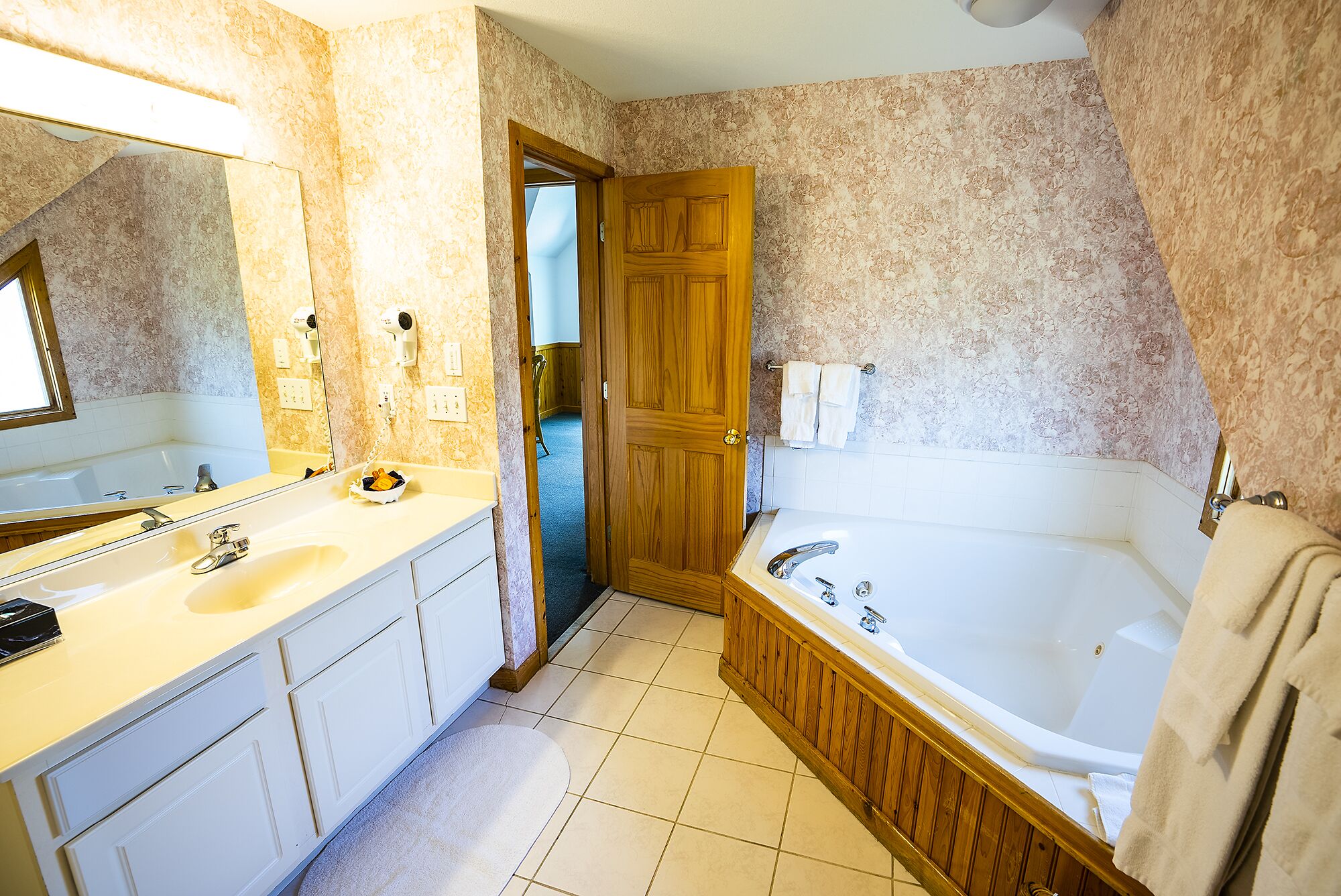 Un baño con una bañera, dos lavamanos, un espejo y una puerta que da a otra habitación.