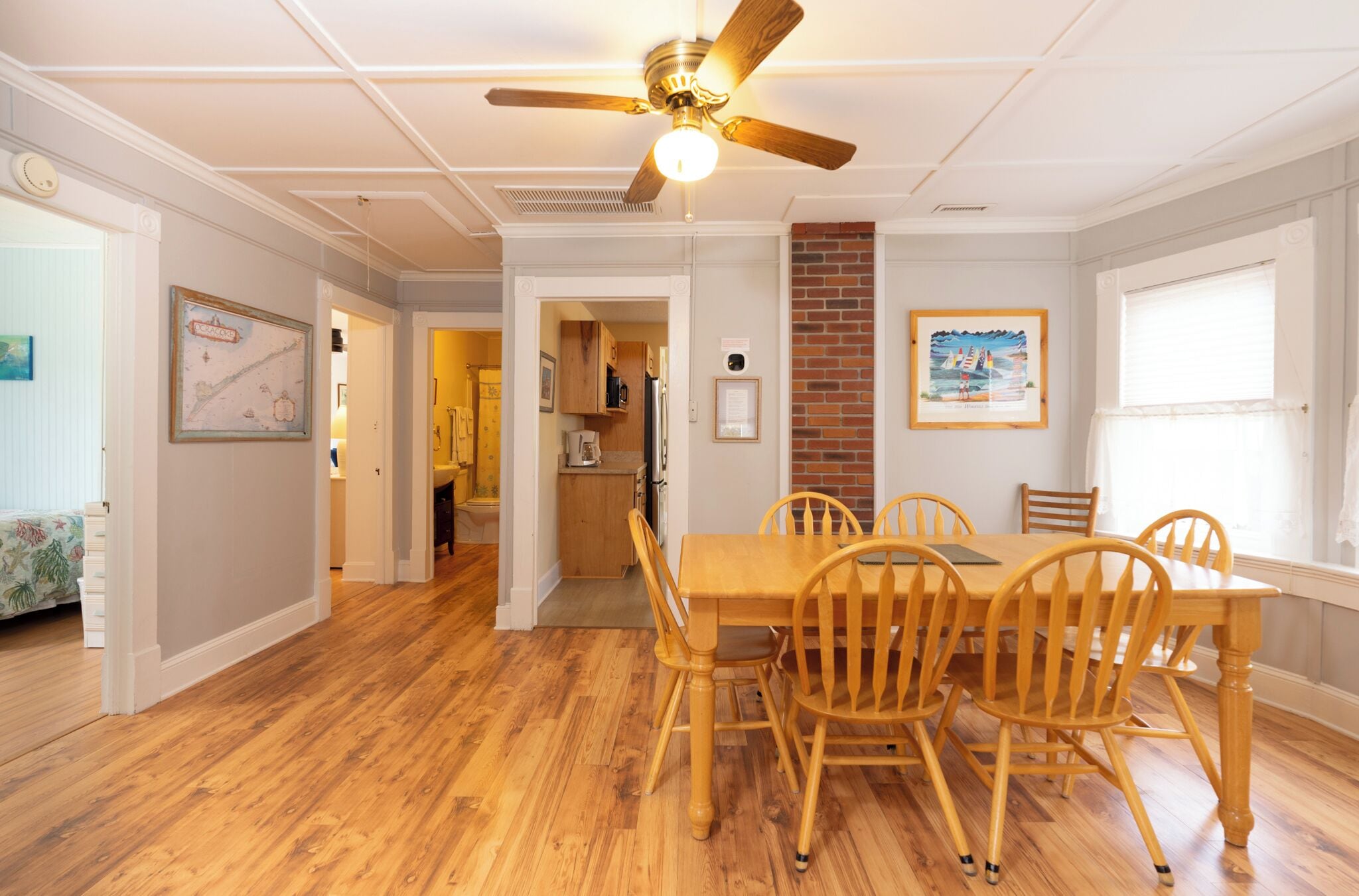 A dining area with a wooden table and chairs, a ceiling fan, and a kitchen in the background.