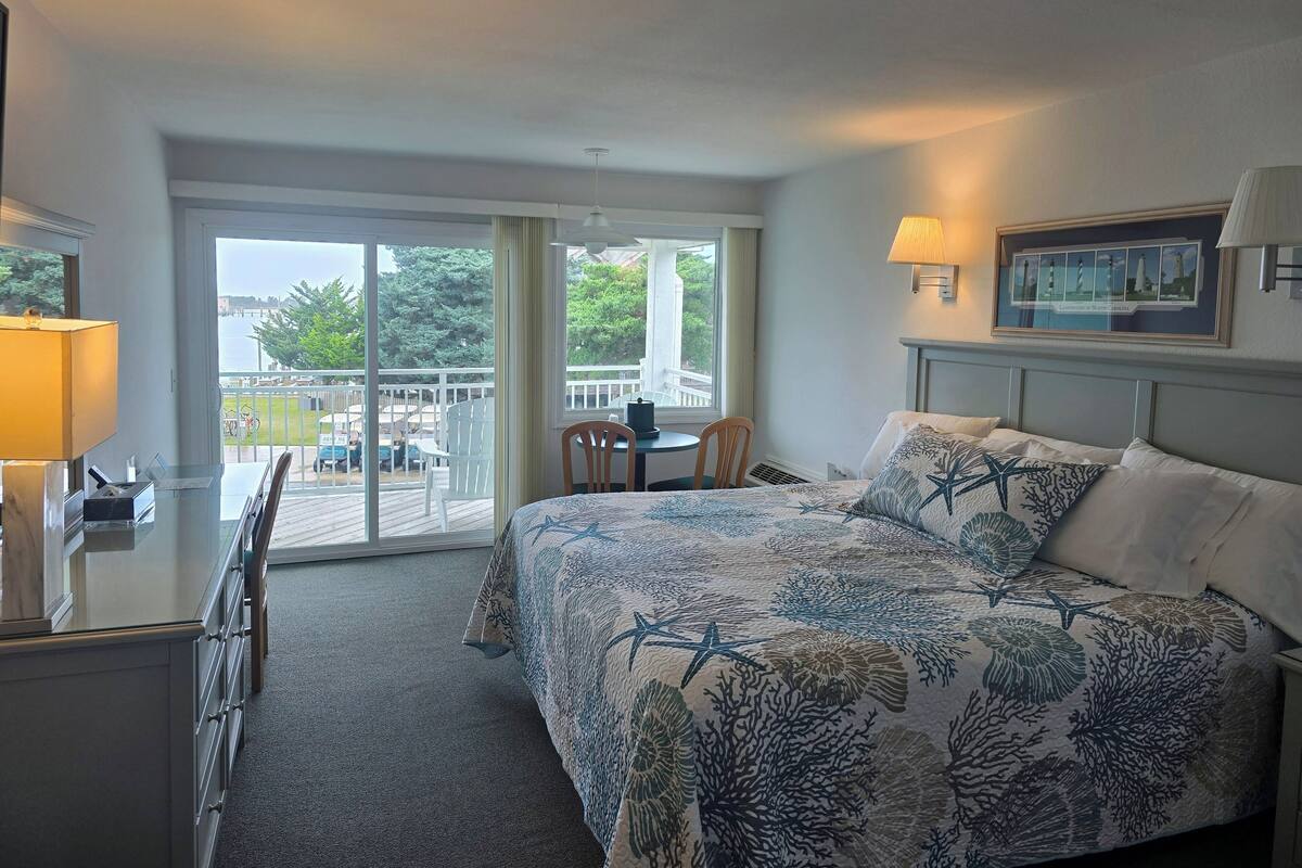 Ein Hotelzimmer mit Bett, Schreibtisch, Stuhl, Tisch und einem Balkon mit Blick auf das Meer und Gebäude.