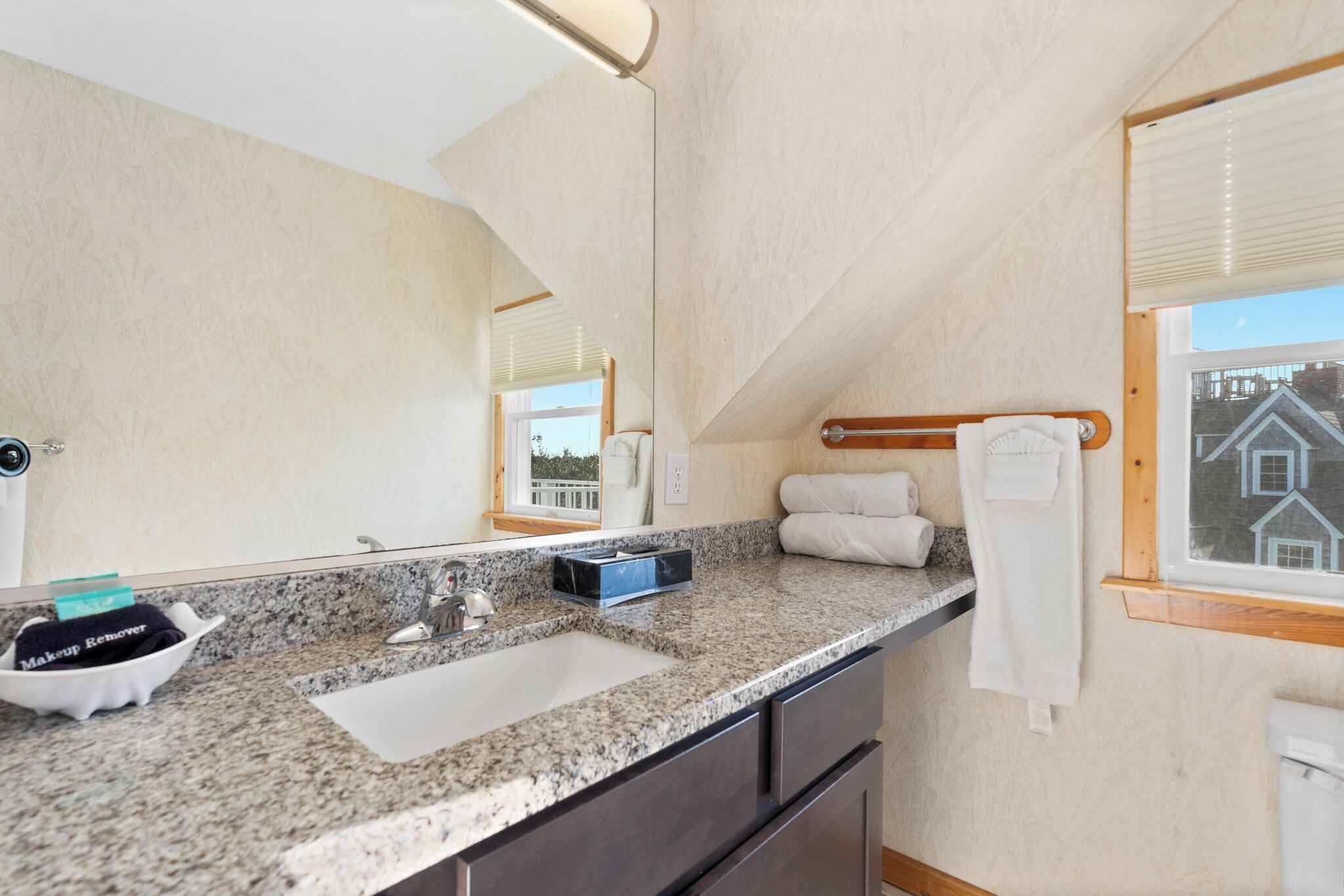 A bathroom with a granite countertop, a sink, a mirror, and a window with a view of buildings.