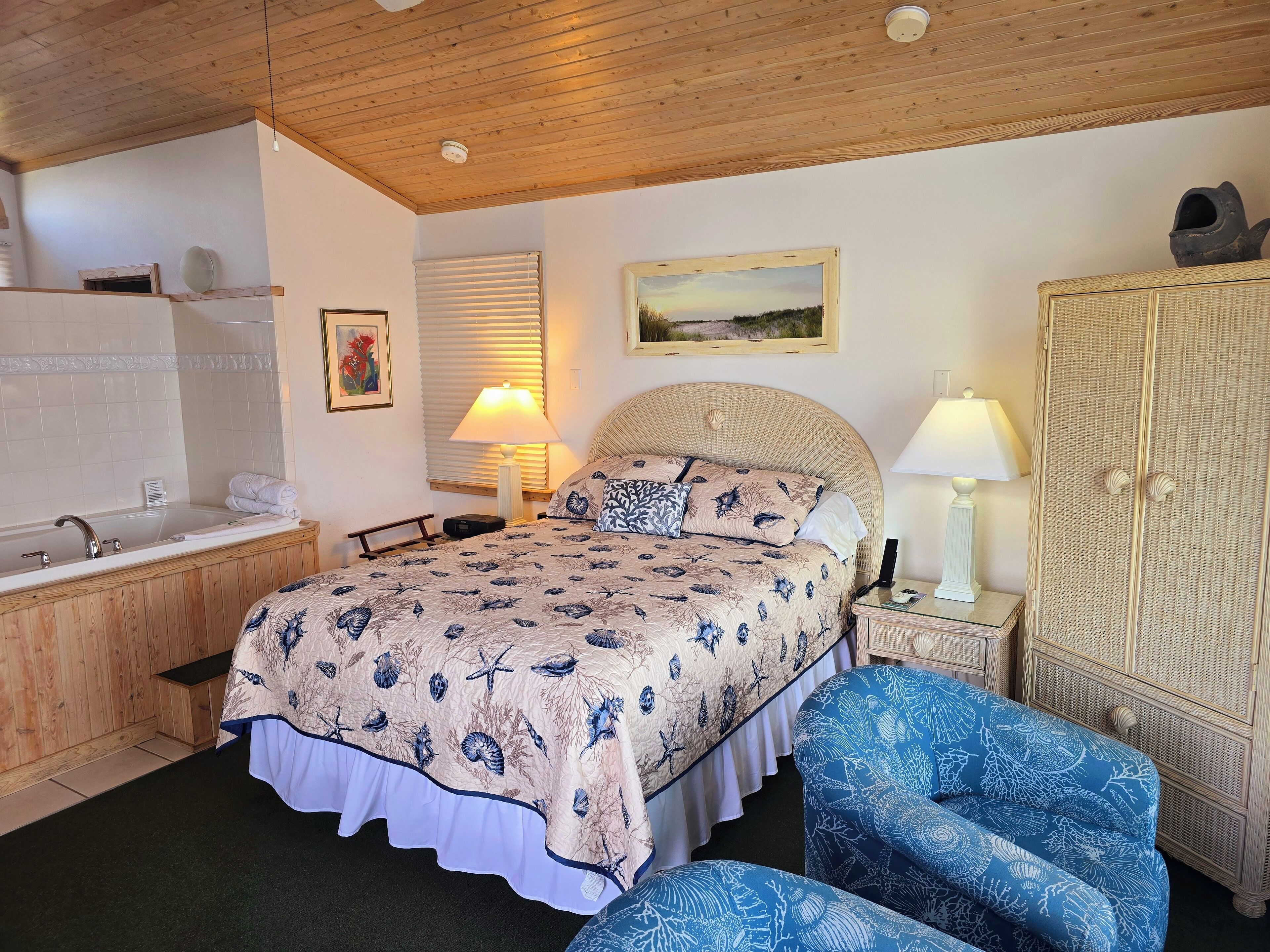 A bedroom with a bed, a nightstand, a lamp, a wardrobe, and a bathroom with a bathtub and a mirror.