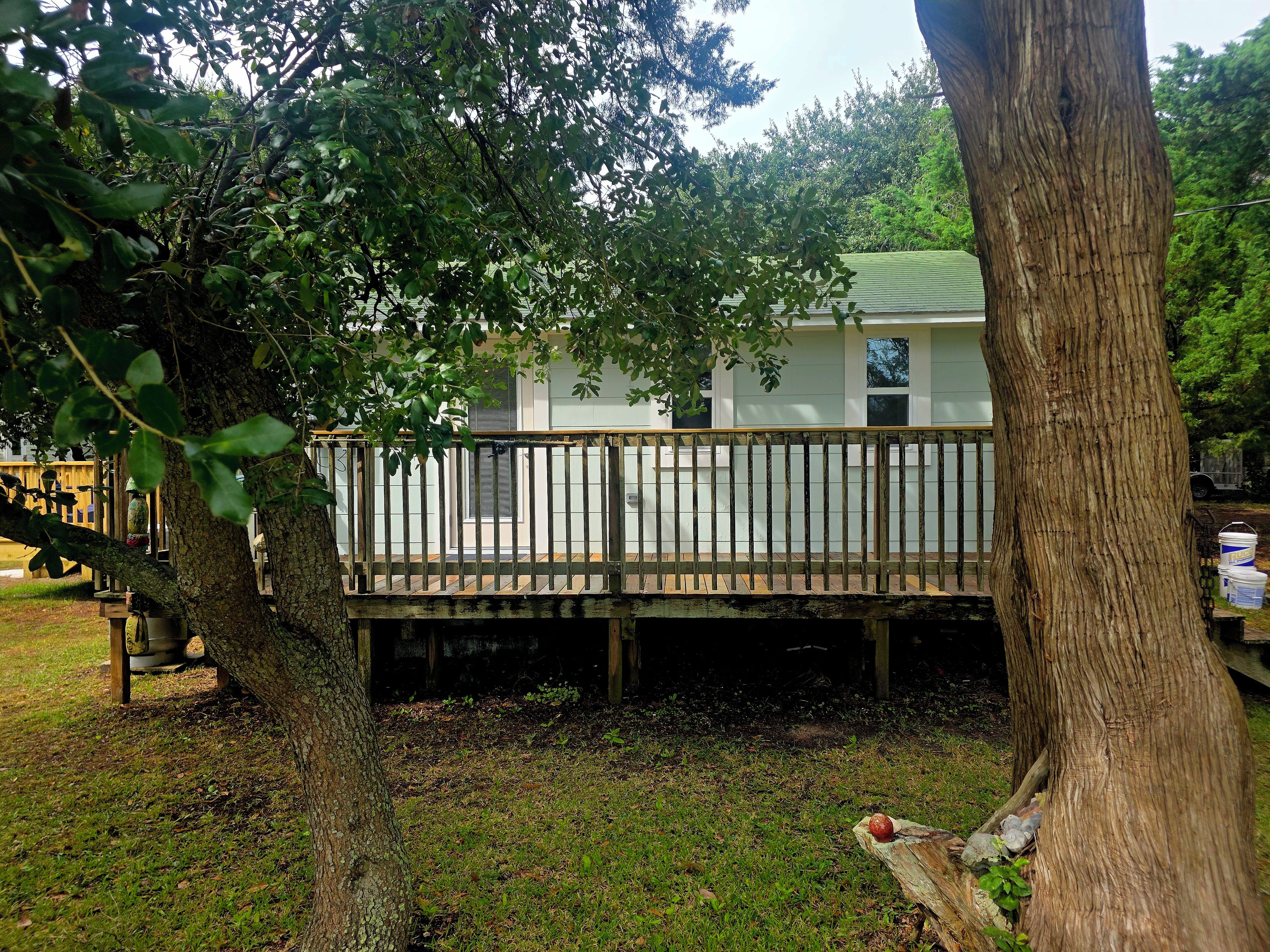 A residential property with a wooden deck, a white house, and a large tree in the foreground.
