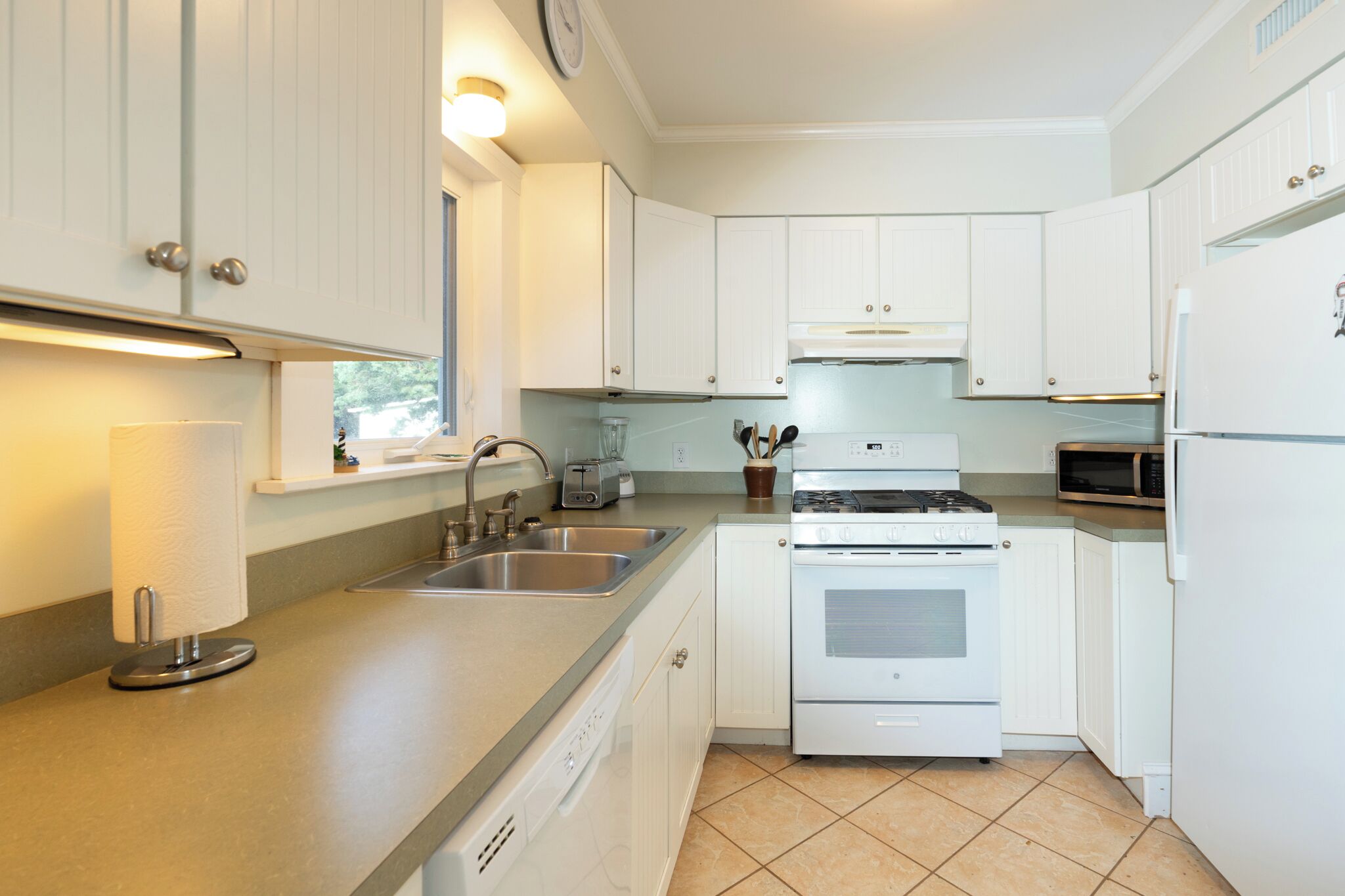 A kitchen with white cabinets, a stainless steel sink, a built-in oven, and a microwave.