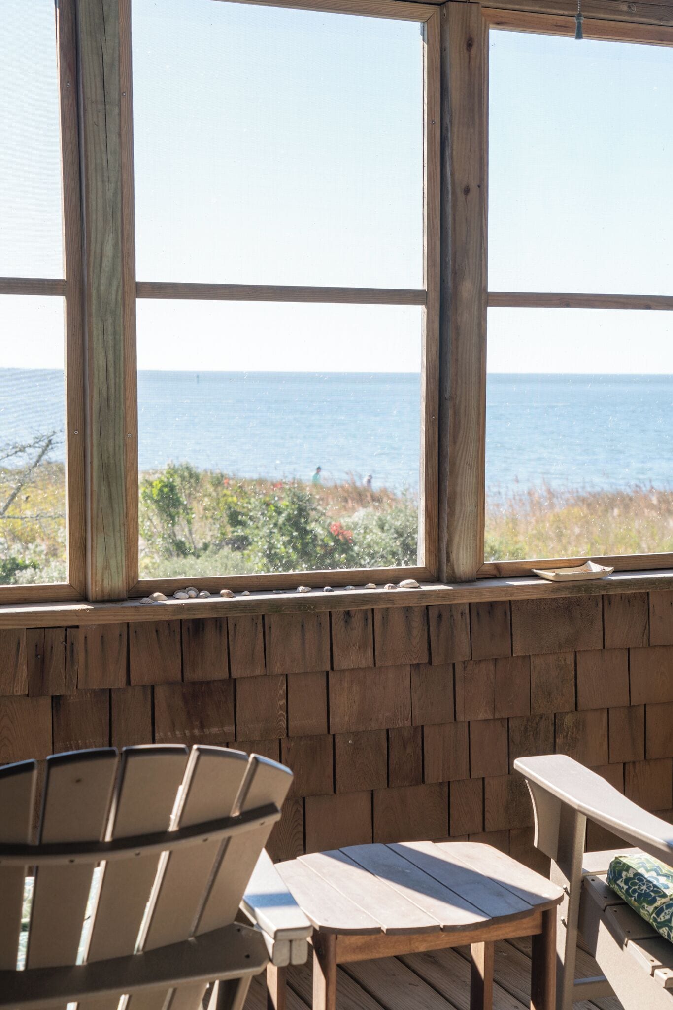 A wooden deck with a view of the ocean, a wooden table, and two chairs.