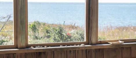 A wooden deck with a view of the ocean, a wooden table, and two chairs.