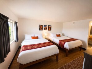 Une chambre d’hôtel avec deux lits simples, un plancher en bois, un bureau et une fenêtre avec des rideaux.
