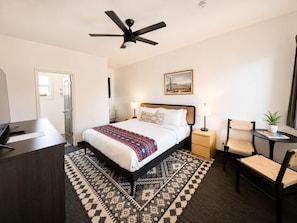 Une chambre d’hôtel équipée d’un lit, d’un bureau, d’une chaise et d’un ventilateur de plafond.