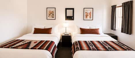Une chambre d’hôtel avec deux lits, un ventilateur de plafond, des œuvres d’art encadrées accrochées aux murs et une fenêtre avec des rideaux.