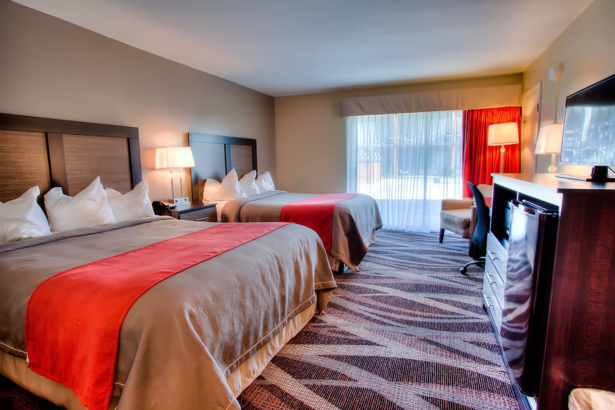A hotel room with two beds, a desk, a television, and a large window with curtains.