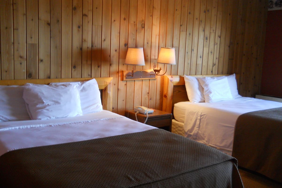 A hotel room with two beds, wooden paneling on the walls, and two bedside lamps.