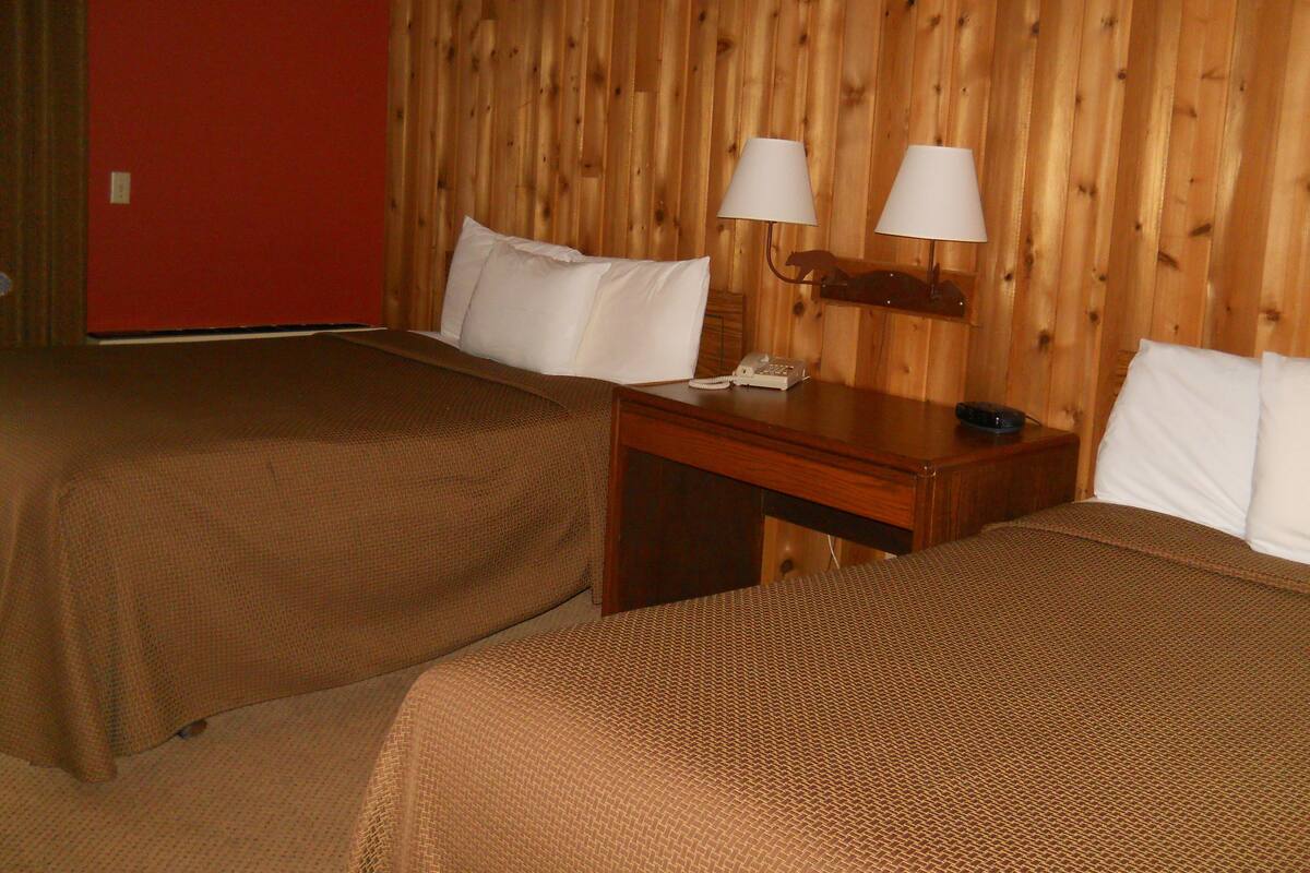 A hotel room with two beds, wooden walls, a desk with a telephone, and lamps.