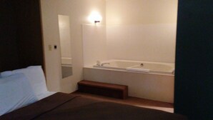 A hotel room with a bed, a bathroom including a bathtub, and a small step leading to the bathroom. - Lakewoods Resort & Lodge (Cable)