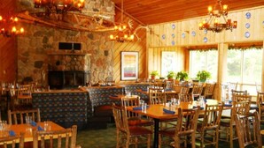 A rustic restaurant interior with wooden tables and chairs, a stone wall, and a fireplace. - Lakewoods Resort & Lodge (Cable)