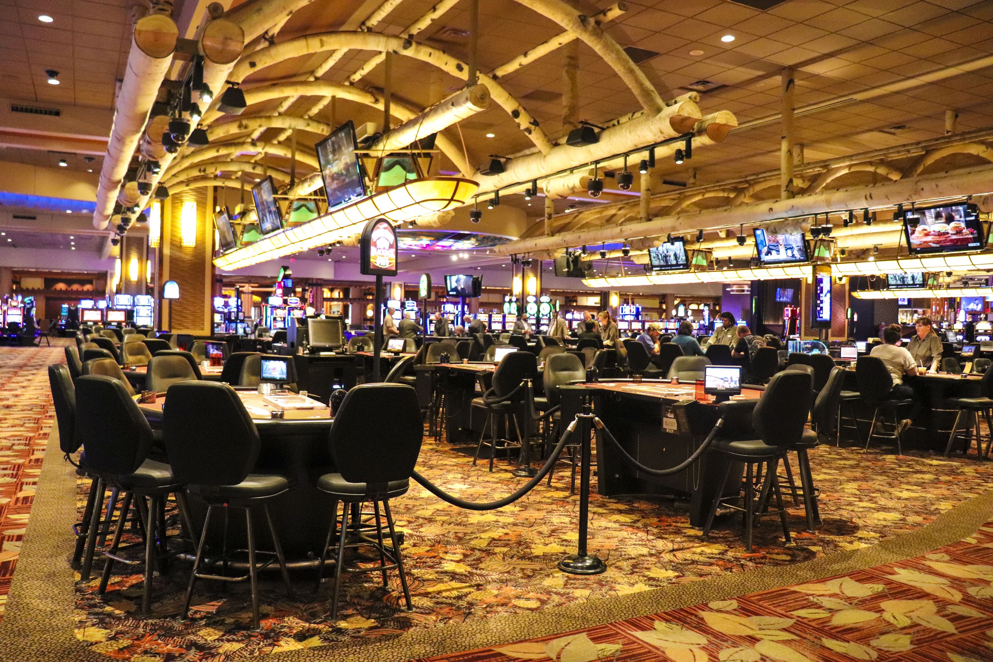 Un casino con varias mesas de juego y sillas, una alfombra estampada e iluminación en el techo.